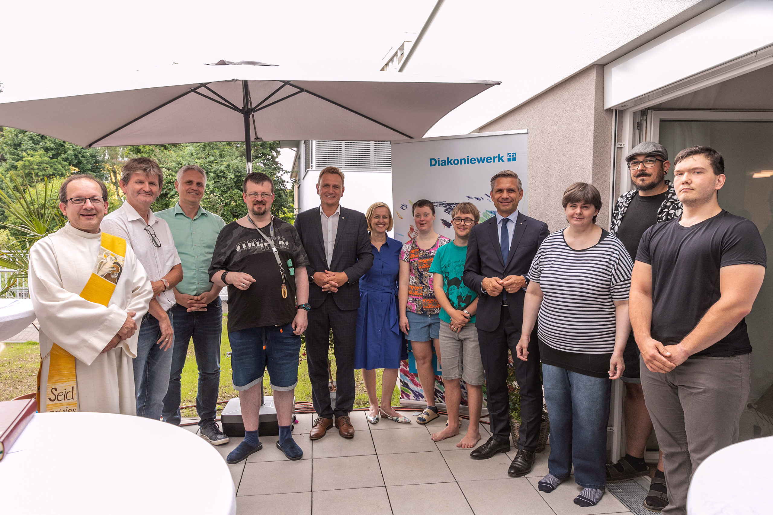 Bewohner/innen mit Ehrengästen bei der Eröffnung der Wohneinrichtung „Begleitet Wohnen Wels“ des Diakoniewerks für Menschen mit Behinderung. Von links: Josef Greifeneder, Mitarbeiter und Diakon; Markus Mayer, Regionalleiter Diakoniewerk; Jürgen Pichler-Stiftinger, Welser Heimstätte; Bewohner; Mag. Klaus Schinninger, VBgm. Stadt Wels; Dr.in Daniela Palk, Vorständin Diakoniewerk; Bewohnerin; Bewohner; Landesrat Dr. Wolfgang Hattmannsdorfer; Bewohnerin; Samir Sassi, Leitung „Begleitet Wohnen Wels“; Bewohner.